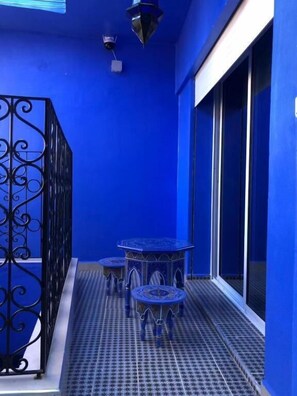 A blue-walled balcony with two small tables and a decorative metal railing.