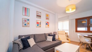 Uma sala de estar moderna com um sofá seccional cinza, uma mesa de centro branca e uma área de jantar com mesa e cadeiras de madeira.