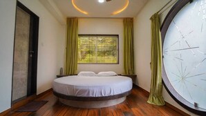 Un lit rond avec un matelas et des oreillers blancs, une fenêtre avec des rideaux verts et un plancher en bois.