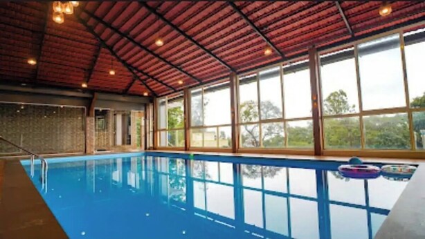 Une piscine intérieure avec un sol bleu, de grandes fenêtres et un toit rouge.