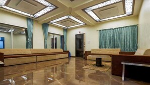 Un vaste espace de vie comprenant un grand canapé, une table basse et un tapis décoratif. La pièce est dotée d’un plafond haut avec des luminaires aux formes géométriques et d’un grand miroir sur l’un des murs.