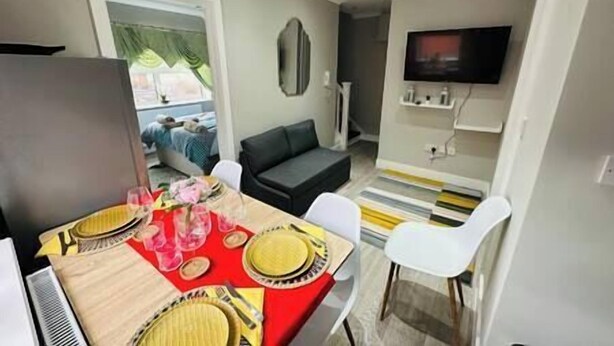 A modern living room with a dining area, a flat-screen TV mounted on the wall, and a sofa. - Spacious and newly built,perfect for your getaway! (Northolt)