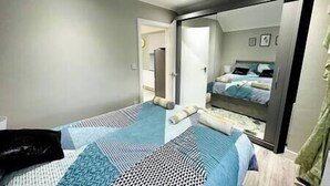 A bedroom with a bed, a mirror, and a door leading to another room. - Spacious and newly built,perfect for your getaway! (Northolt)