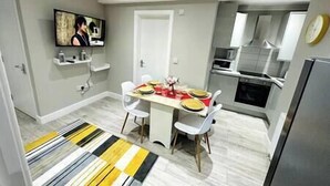 A modern kitchen with white cabinets, a stainless steel refrigerator, and a dining area with a striped rug. - Spacious and newly built,perfect for your getaway! (Northolt)