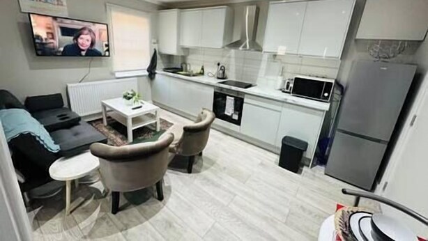 A modern kitchen with white cabinets, a microwave, and a refrigerator. There is a small dining area with a table and chairs. - Stylish and Luxury Flat in LND (Uxbridge)