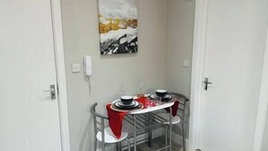 A small dining area with a table set for two, a painting on the wall, and a door to the right. - Stylish and Luxury Flat in LND (Uxbridge)