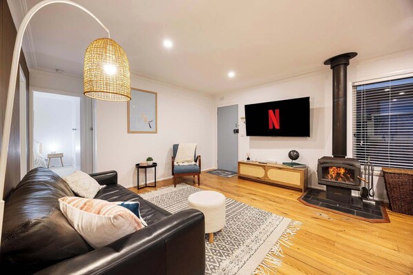 Ein modernes Wohnzimmer mit einer Ledersofa, einem an der Wand montierten Fernseher, einem Kamin und einem großen Fenster mit Jalousien.