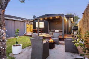 Ein Patio mit Gartenmöbeln aus Rattangeflecht, einer Feuerstelle und einem überdachten Sitzbereich.