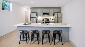 A modern kitchen with grey cabinets, stainless steel appliances, a white island with bar stools, and a "HELLO" sign. - Relaxing unit near Louisville Medical Complex! (Louisville)