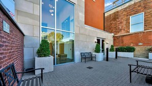 A courtyard with a brick building, glass doors, benches, and potted plants. - Relaxing unit near Louisville Medical Complex! (Louisville)