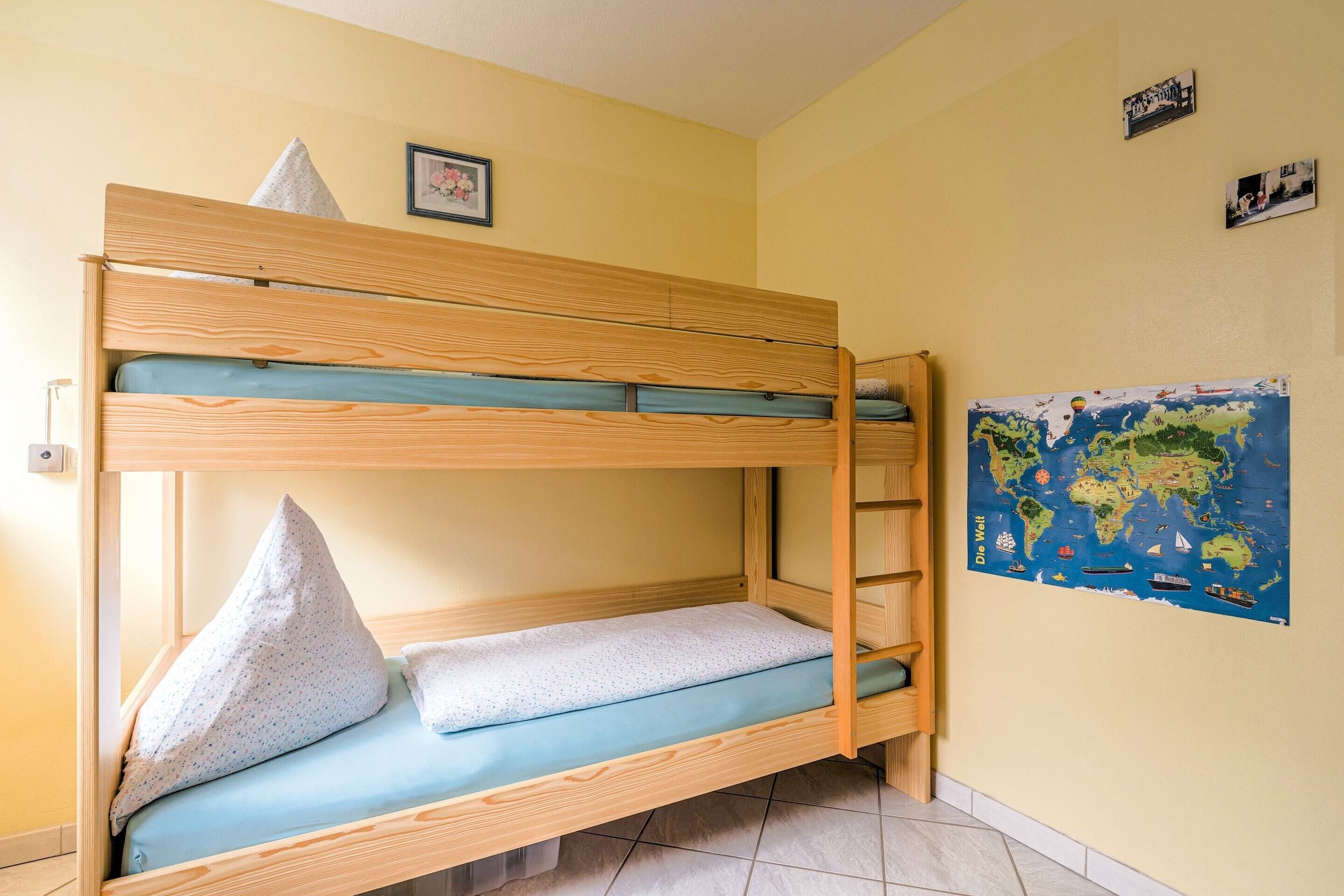 A bunk bed with a blue mattress and pillows, a wooden ladder, and a world map on the wall.