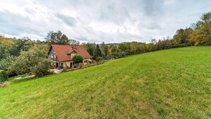 A house with a red roof, surrounded by a grassy field and trees. - Cozy Apartment in Marktrodach With Sauna (Marktrodach)