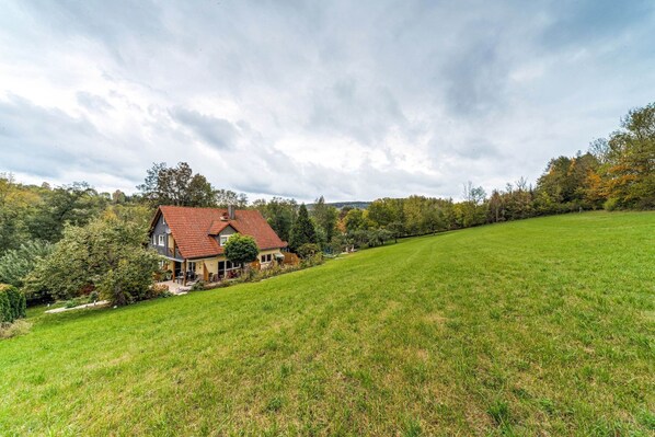 A house with a red roof, surrounded by a grassy field and trees. - Cozy Apartment in Marktrodach With Sauna (Marktrodach)