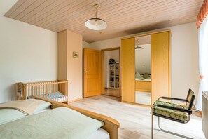 A bedroom with a wooden crib, a bed, a green upholstered chair, and a wardrobe with a mirror. - Cozy Apartment in Marktrodach With Sauna (Marktrodach)