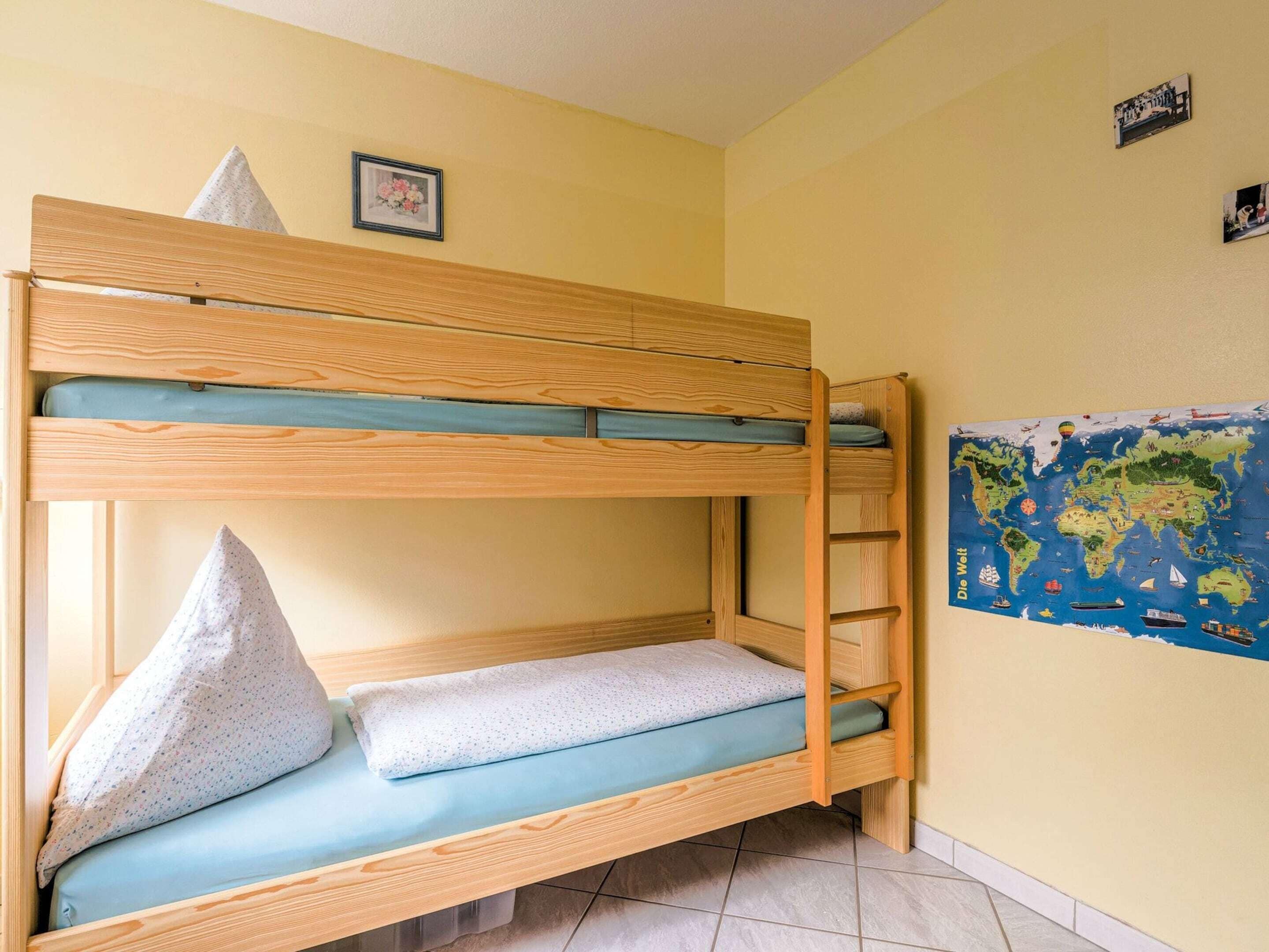 A bunk bed with a ladder, a pillow, and a world map on the wall.