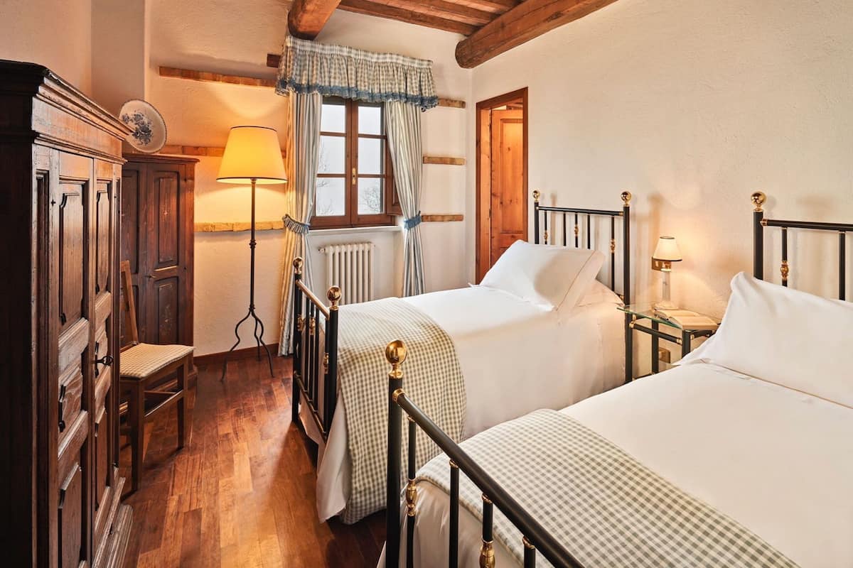 Une chambre traditionnelle avec deux lits simples, une armoire en bois, une petite table et une chaise.