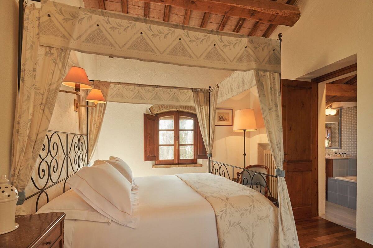 Un lit à baldaquin, deux lampes de chevet, un plafond en bois et une vue sur la salle de bain par une porte ouverte.