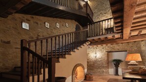 Un interior rústico con una escalera de madera, paredes de piedra y una chimenea.