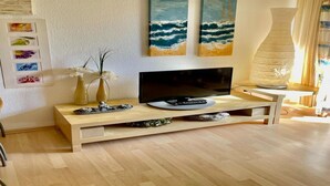 Una sala moderna con un mueble de televisión de madera, un televisor de pantalla plana y dos cuadros con motivos playeros.