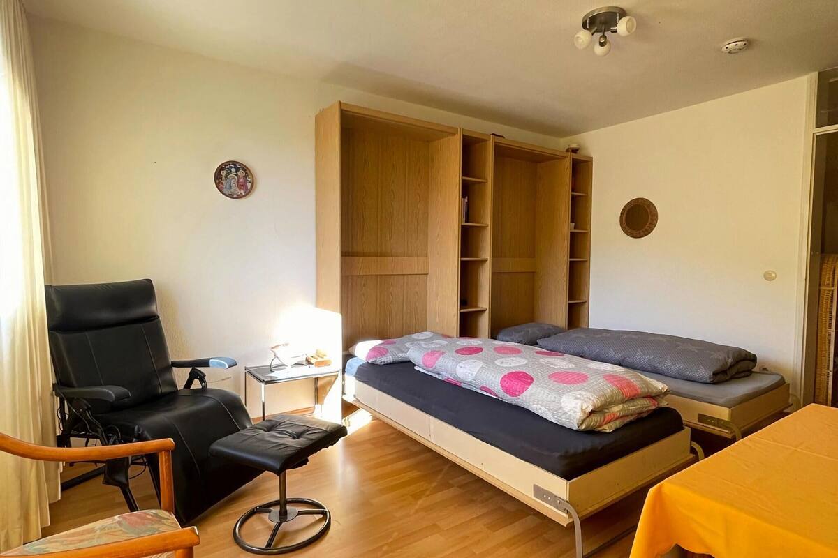 Habitació senzilla amb llit, cadira, taula petita i armari.