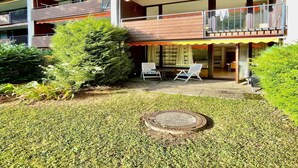 Un edificio residencial de varios pisos con balcones, un pequeño patio con dos sillas y un césped bien cuidado.