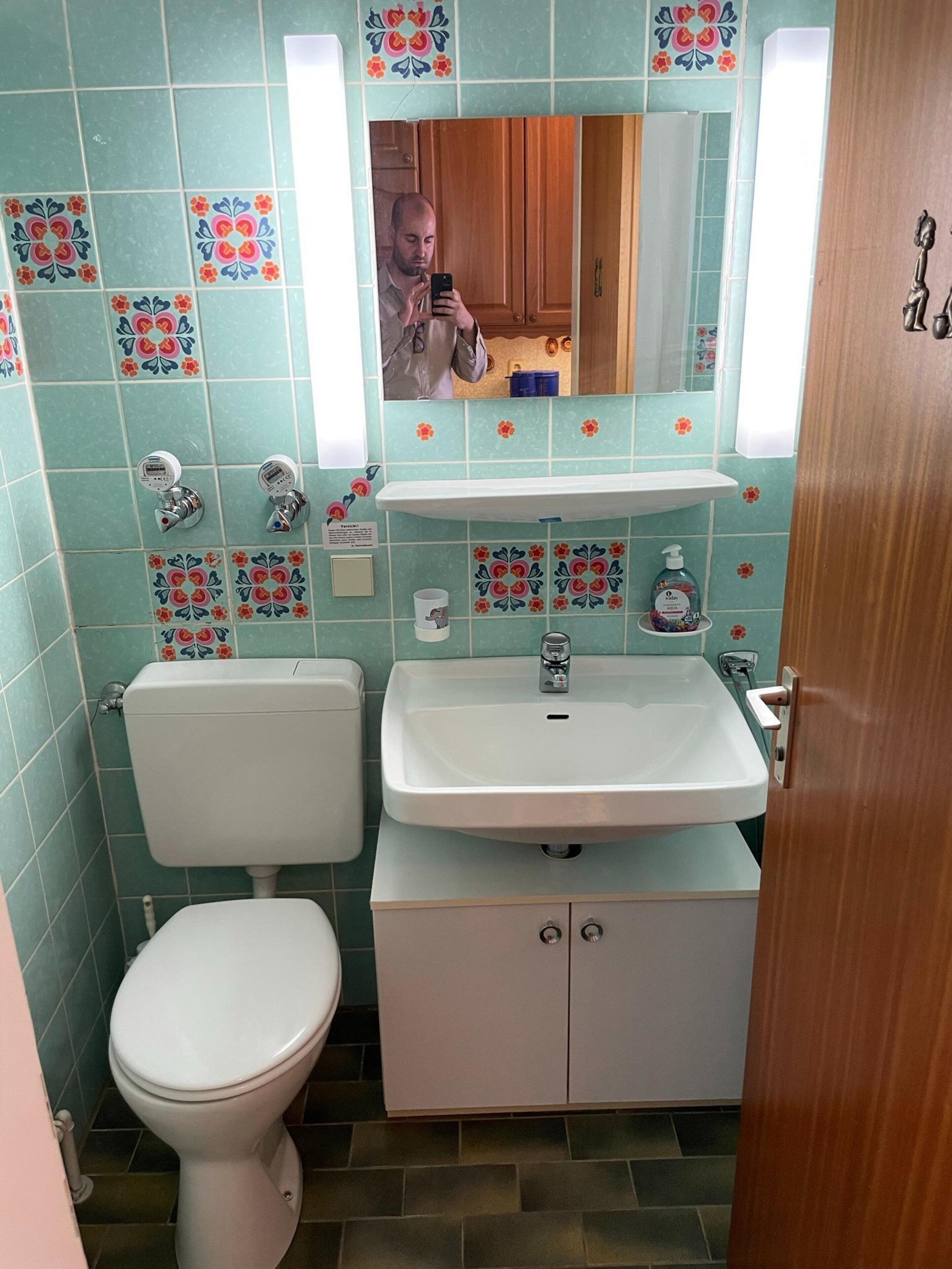 A bathroom with a toilet, sink, and mirror.