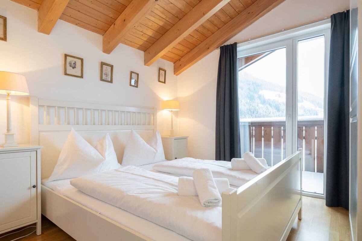 A bedroom with a large bed, two bedside tables, a headboard, and a view of a snowy landscape through a window.