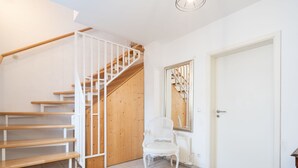 Una escalera de madera con barandillas blancas, una silla blanca y una puerta con un espejo que refleja la escalera.