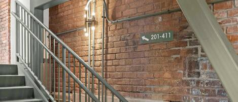 Una escalera con barandales metálicos y un muro de ladrillo. Se ve un letrero con el número "201-411".