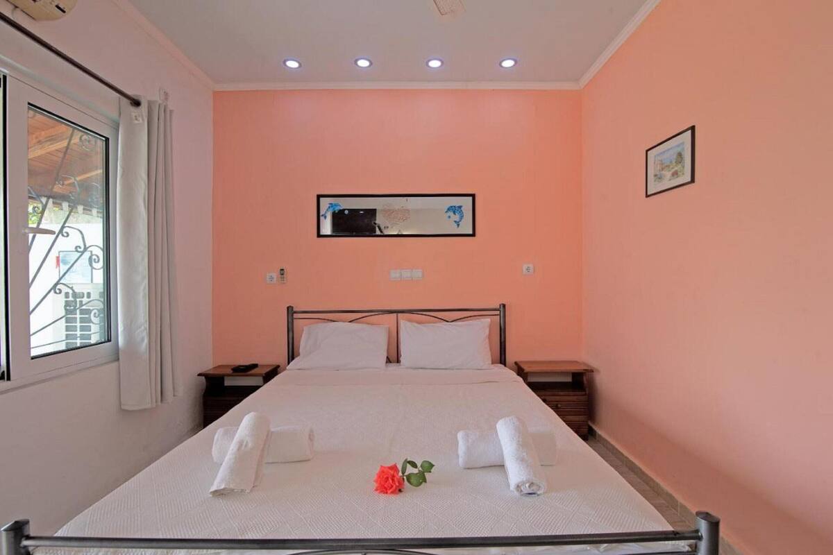 A neatly made bed with white linens, a single red rose, and two bedside tables with lamps.