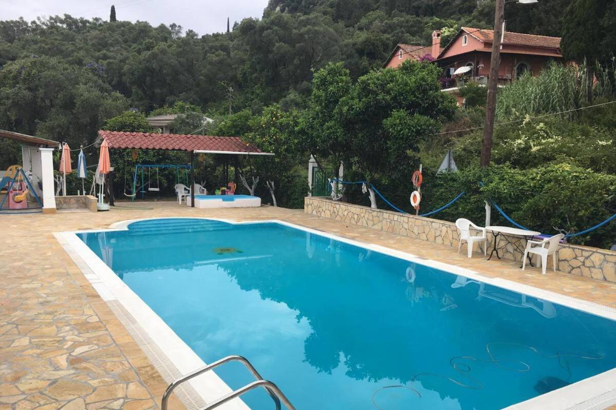 A rectangular swimming pool with a stone border, a lifeguard stand, and a small covered seating area with umbrellas.