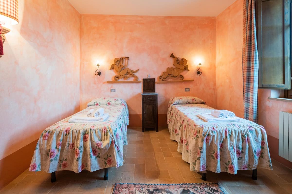 A room with two beds, each with floral bedding, a central wooden cabinet, and wall-mounted sconces.