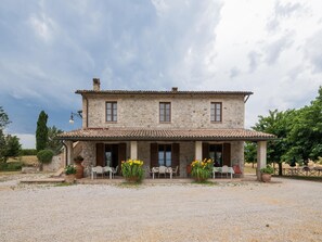 A two-story stone building with a tiled roof, a covered porch with outdoor seating, and a gravel driveway. - Apartment in Villa With Swimming Pool (Fabro)
