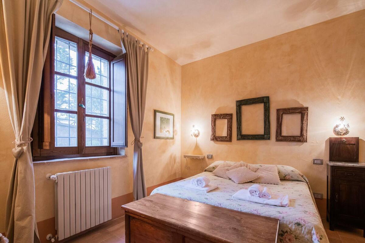A bedroom with a wooden bed, a radiator, a window with curtains, and wall-mounted picture frames.