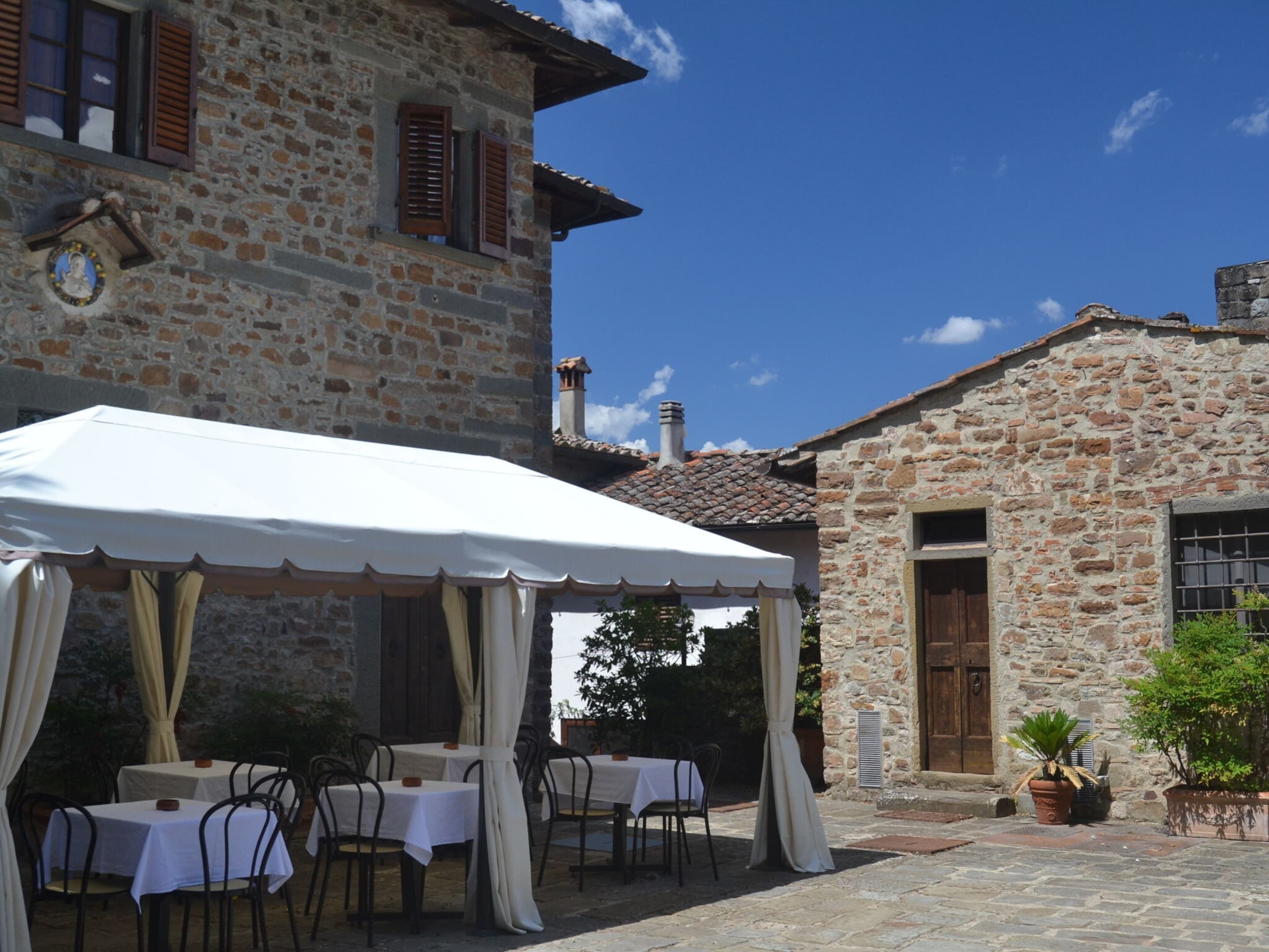 A stone building with a white outdoor seating area featuring tables and chairs.
