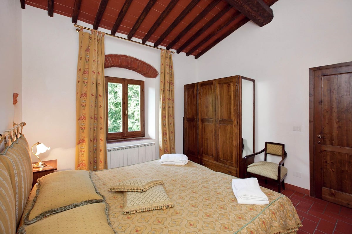 A bedroom with a bed, a chair, a wardrobe, a window with curtains, and a door.