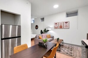 A modern kitchen with a stainless steel refrigerator, a dining table with a 'HELLO' sign, and a sofa in the background.