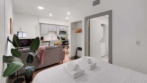 A modern hotel room with a bed, a sofa, a dining area, and a kitchen.
