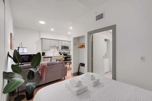 A modern hotel room with a bed, a sofa, a dining area, and a kitchen.