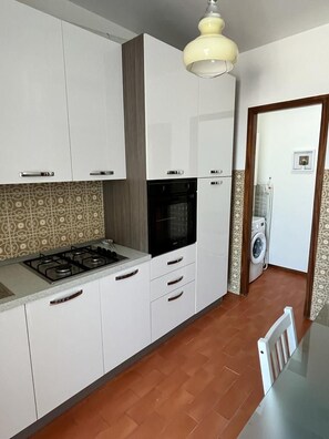 A kitchen with white cabinets, a gas stove, and a microwave. - Terrazza sul Mare (Marina Julia)