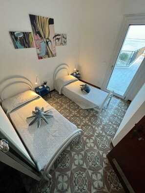 A room with two beds, a small table with a lamp, and a window. - Terrazza sul Mare (Marina Julia)