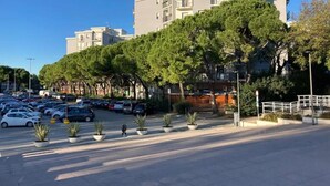 Un parking rempli de voitures, une rangée de plantes en pot et, au fond, un immeuble avec des balcons.