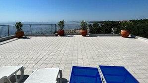 Une terrasse avec un sol carrelé, des plantes en pot et une vue sur la mer.