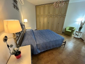 Un dormitorio con una cama, lámparas de noche, una planta en maceta, un armario y una silla verde.