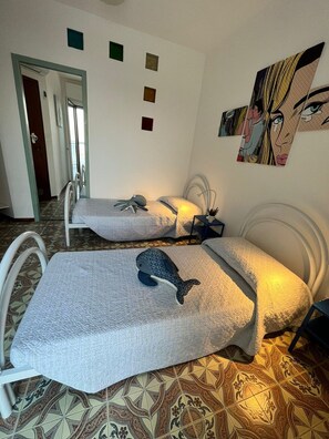 A room with two beds, a patterned floor, a door, and a wall with a painting. - Terrazza sul Mare (Marina Julia)
