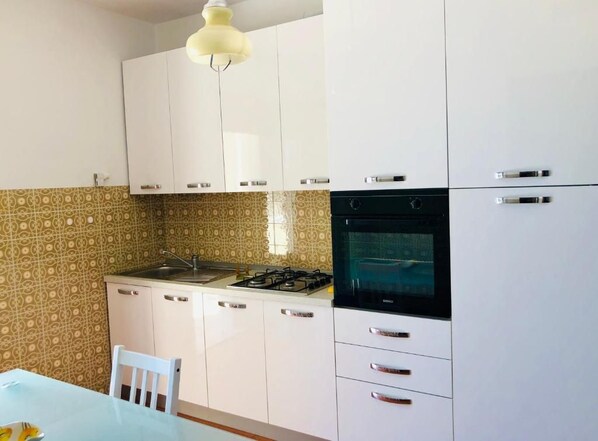 A kitchen with white cabinets, a gas stove, an oven, and a sink. - Terrazza sul Mare (Marina Julia)