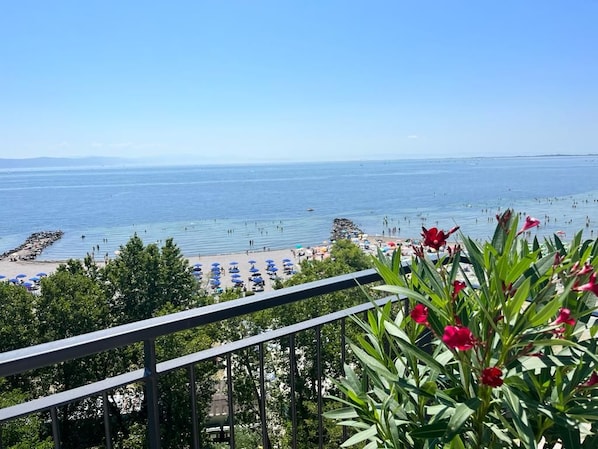 Vista a la playa desde un balcón con barandilla, que domina una playa arenosa con sombrillas y gente.