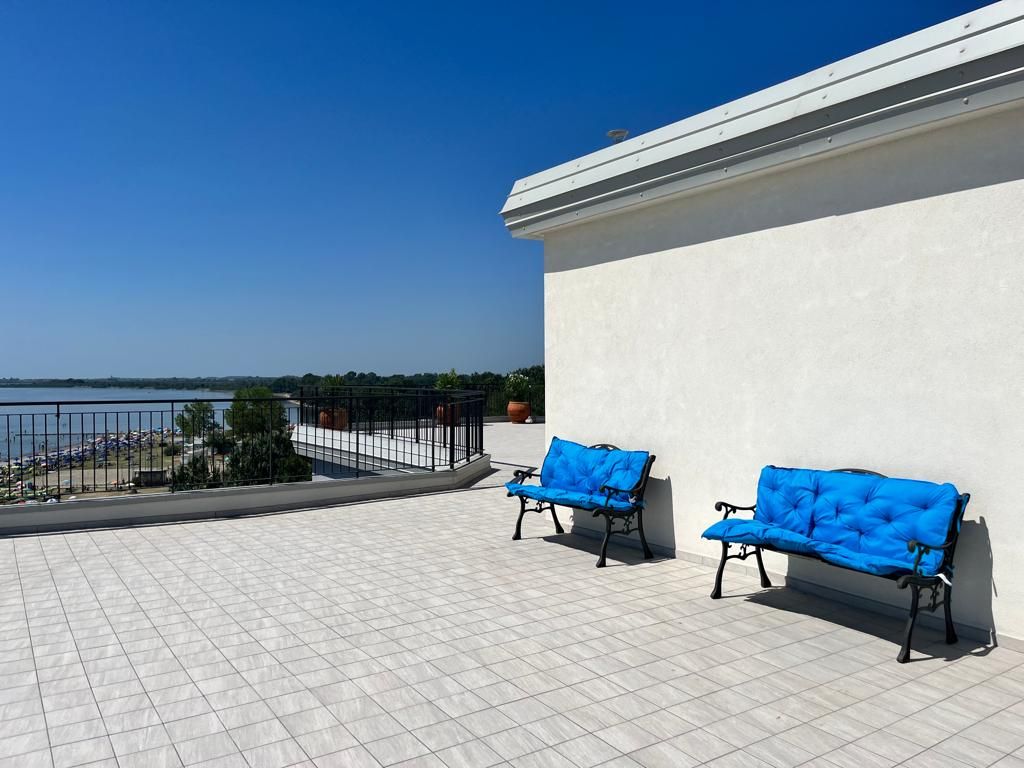 A balcony with two blue cushioned chairs, a white wall, and a view of a body of water.