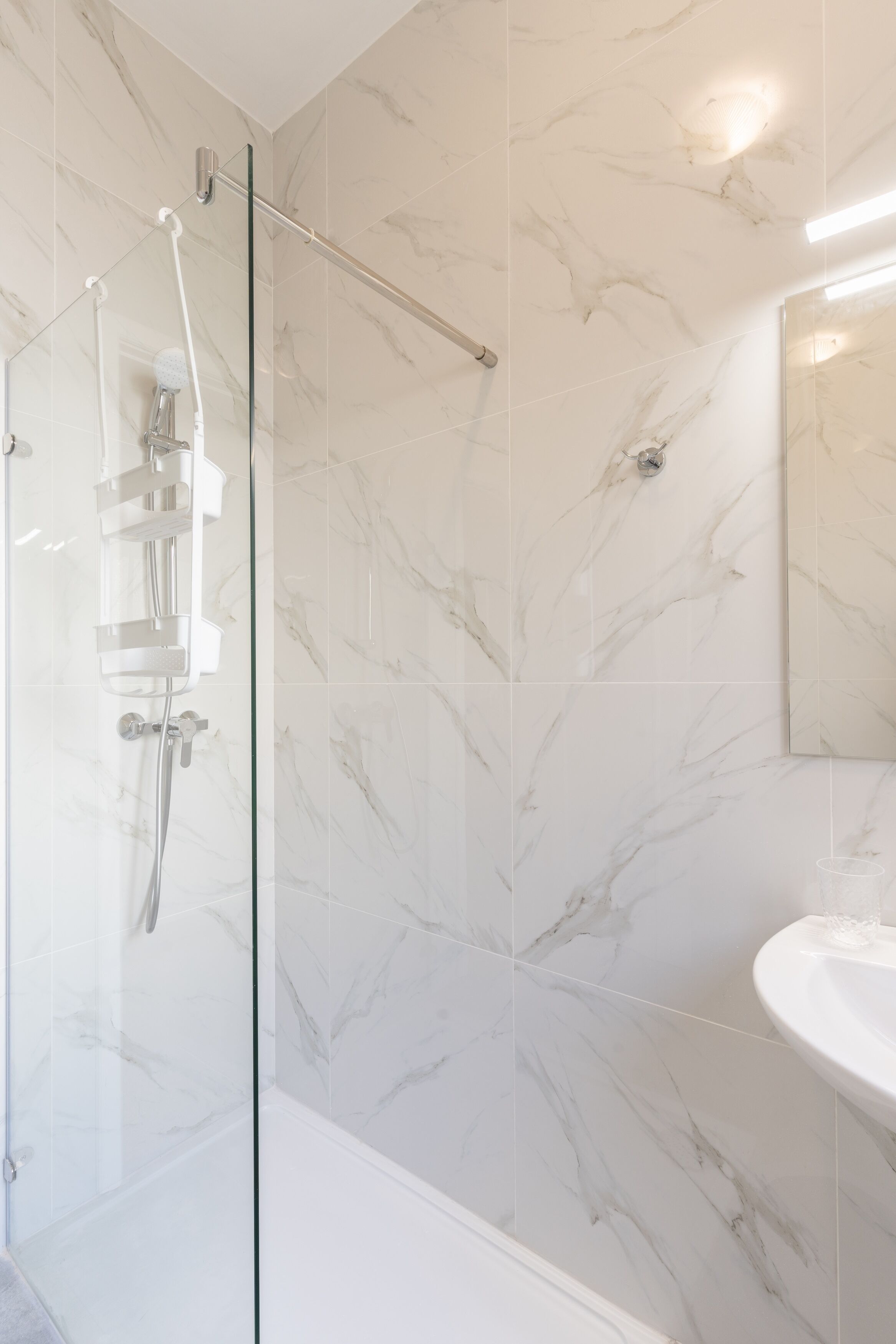 A modern bathroom with a glass-enclosed shower, a white sink, and marble-patterned walls.