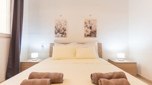 A hotel room with a large bed, two bedside tables with lamps, and two wall-mounted artworks. - Tempo Suites (St. Paul's Bay)